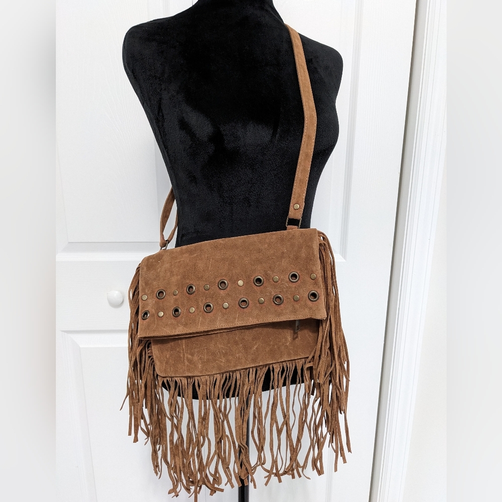 Suede crossbody bag with tinsels around. Brass metal details in front.